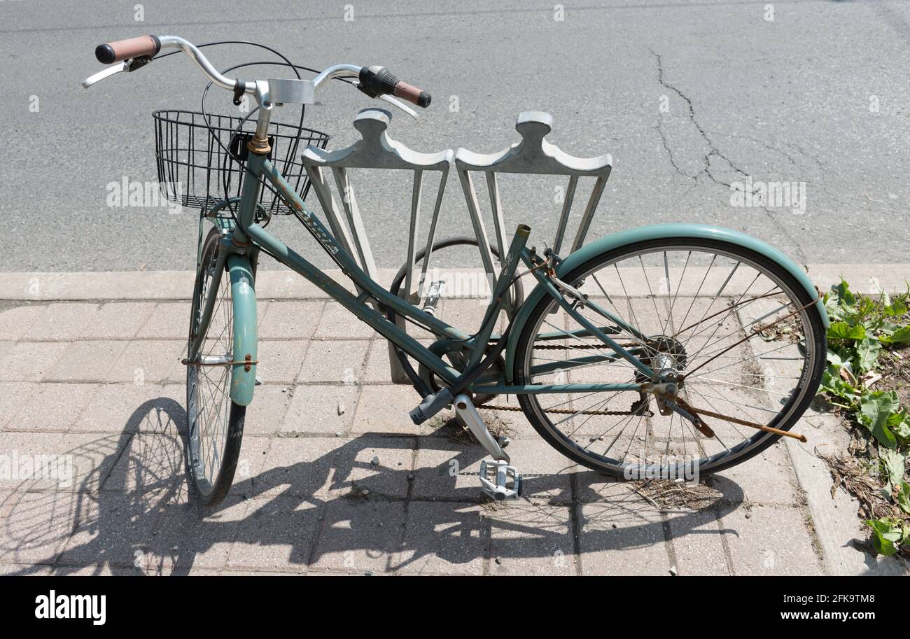 Hellblaues Fahrrad mit Cruiser-Lenker, Vorderkorb, aber fehlenden Sitz - aufgegeben an einem Stadtradschloss Stockfoto
