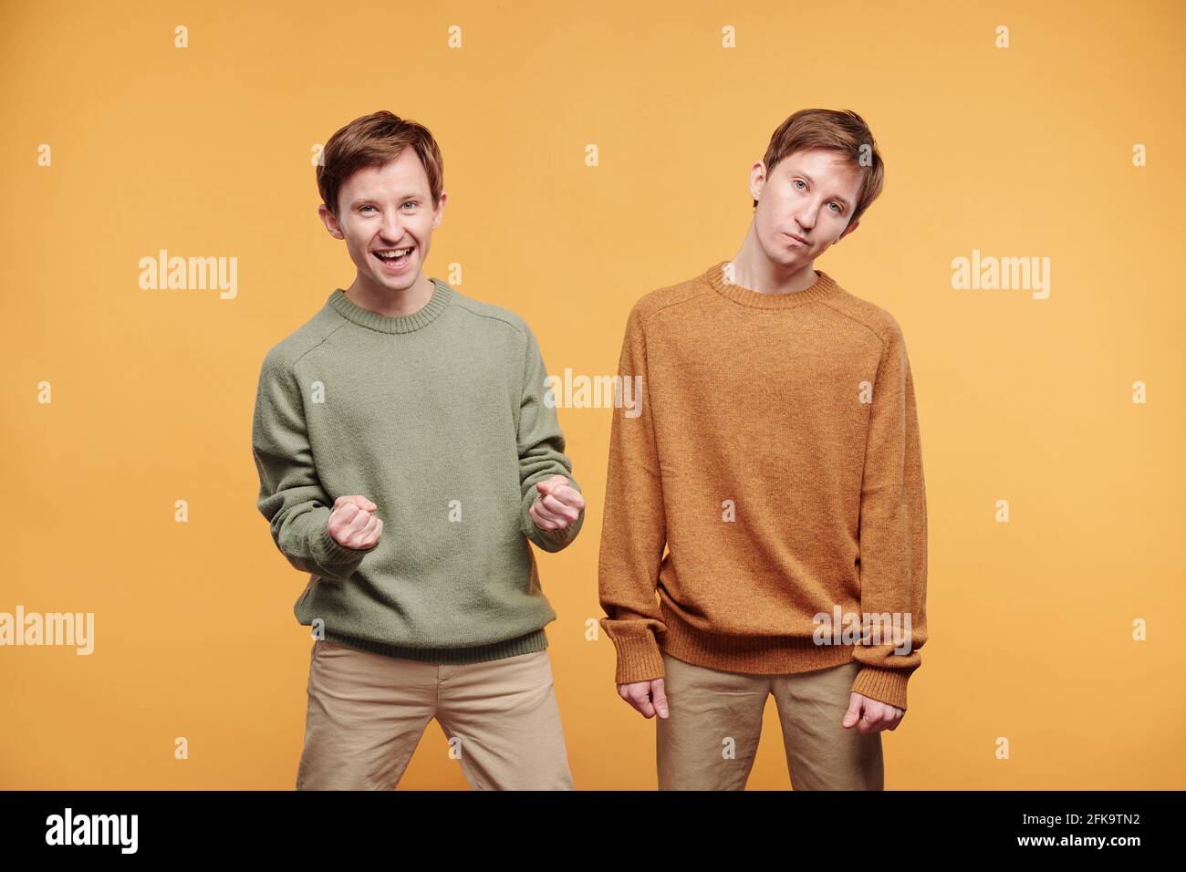 Portrait von jungen Zwillingen mit unterschiedlichen Emotionen: Aufgeregter Mann, der ja-Geste macht, während sein Bruder langweilig aussieht Stockfoto