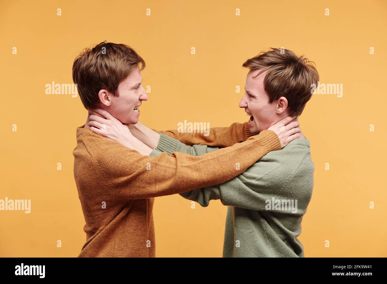 Zornige Zwillinge in Pullovern, die sich vor orangefarbenem Hintergrund ersticken Stockfoto