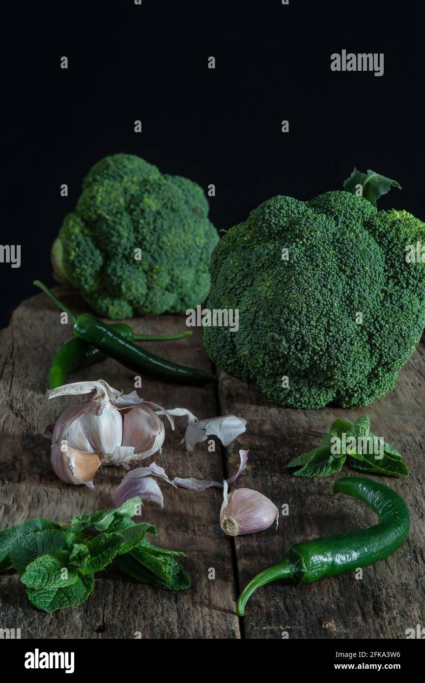 Stillleben mit grünem Brokkoli, Chilies, Knoblauch und Minze auf Holzbrett Stockfoto