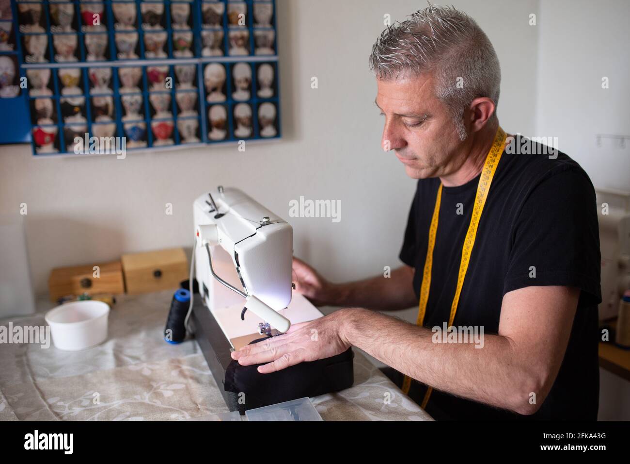 Ein Schneider, der mit seiner Nähmaschine in seinem kleinen arbeitet Aufbau des Workshops Stockfoto