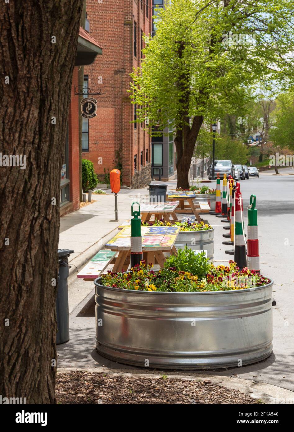ASHEVILLE, NC, USA-25 APRIL 2021: Große bunte Blumentöpfe aus Edelstahl und Picknicktische Reihen sich vor Penny Cup Coffee Co., in der Innenstadt, an. Stockfoto