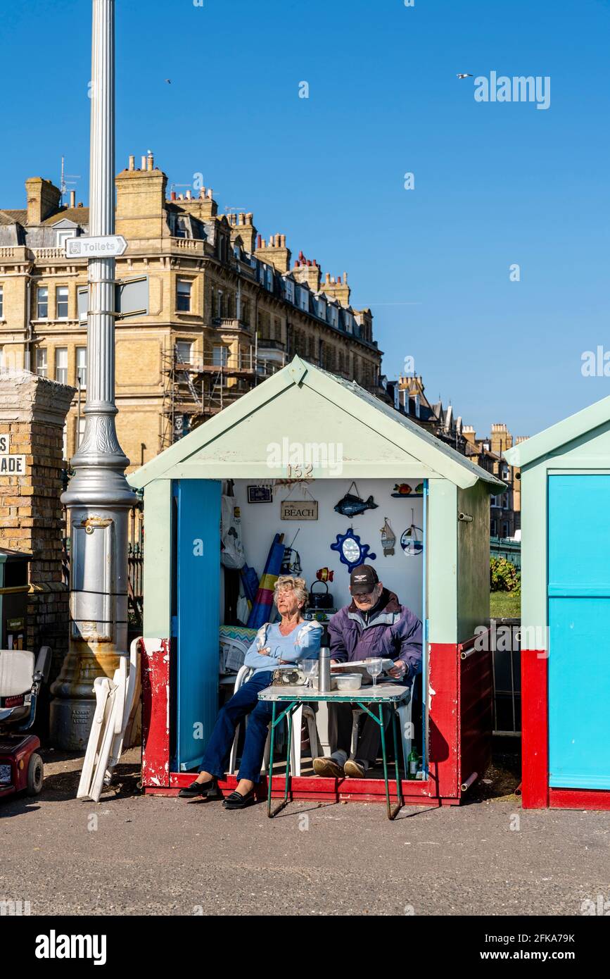 Ein älteres Paar, das vor der Strandhütte an der Hove Seafront, Brighton, East Sussex, Großbritannien, sitzt. Stockfoto