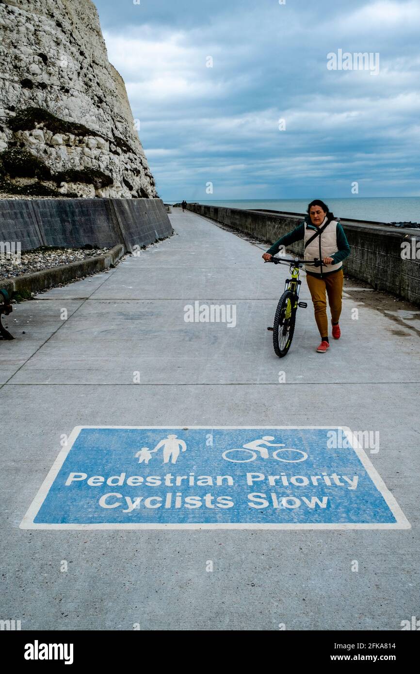 Eine Radfahrerin steigt am Undercliff Walk, Rottingdean, (nahe Brighton) East Sussex, Großbritannien, aus. Stockfoto