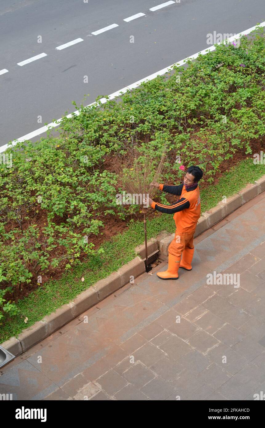 Senayan, Jakarta, Indonesien - 23. April 2021: Ein Straßenreiniger in Orange säugt seine Ausrüstung. Stockfoto
