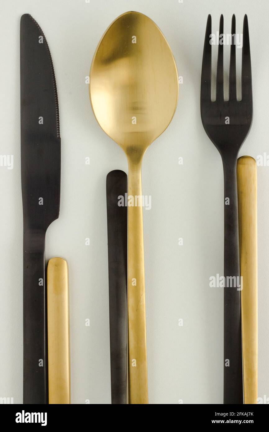 Goldene und schwarze Gabel, Messer und Löffel auf weißem Hintergrund; Art déco; Bestecksdesign; Besteck flach liegend; kreativ Stockfoto