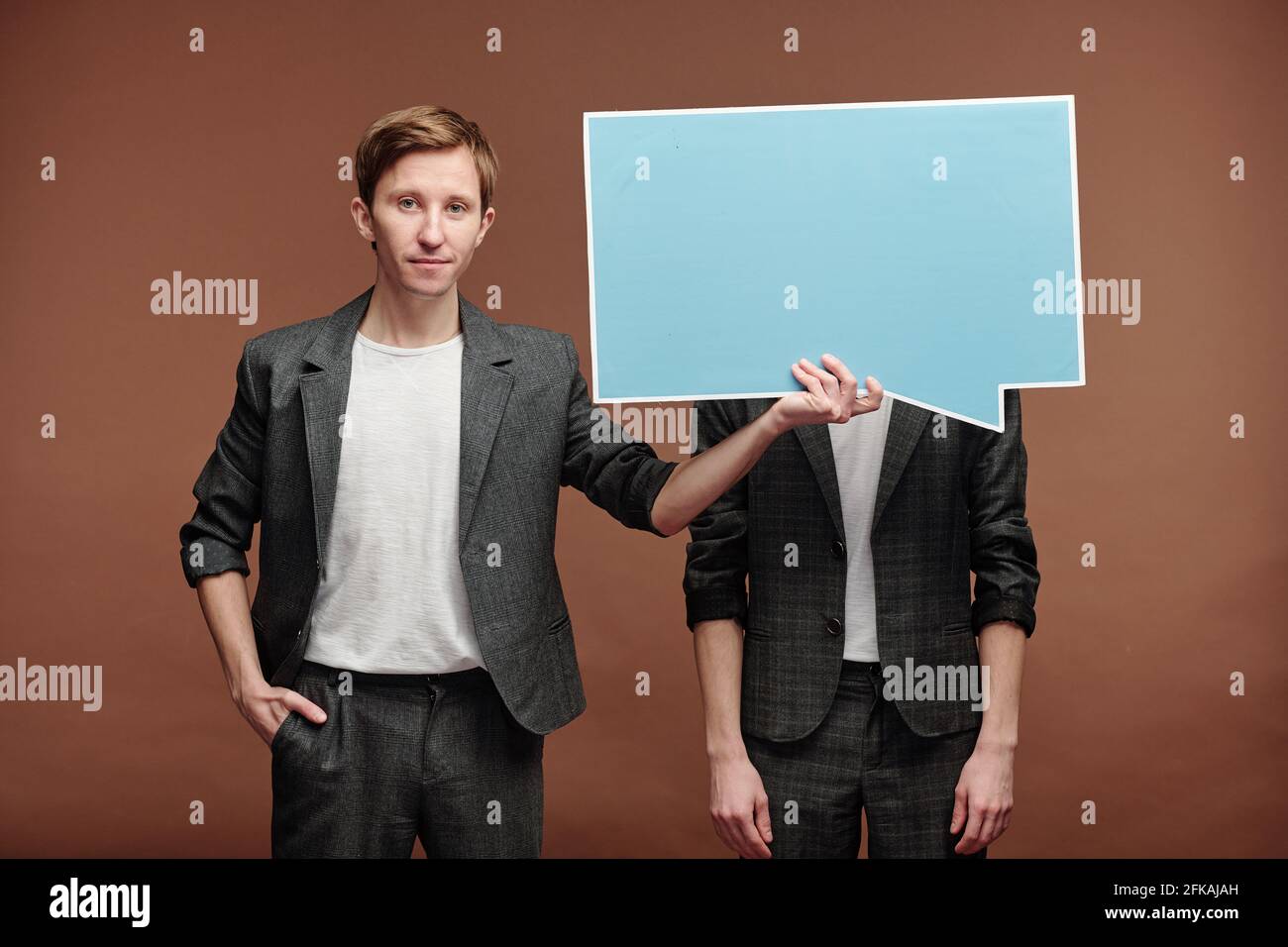 Porträt des Inhalts junger Mann in smart casual Anzug versteckt Gesicht des Mannes hinter Sprechblase Tag vor braunem Hintergrund Stockfoto