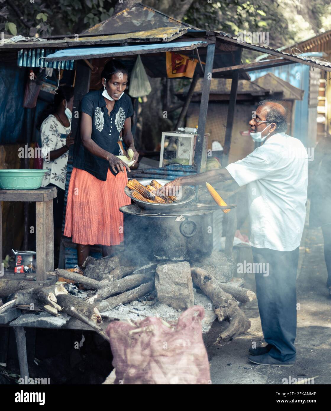 Ella, Sri Lanka - 04 15 2021: Kauf von Street Food in der Nähe von Rawana Ella von einer lokalen Verkäuferin von einem Mann mit Gesichtsmaske, Verkauf von köstlichen gekochten und gr. Stockfoto