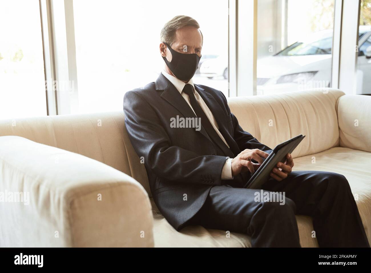 Ernsthafter Mann, der sein Tablet in der Lobby benutzte Stockfoto