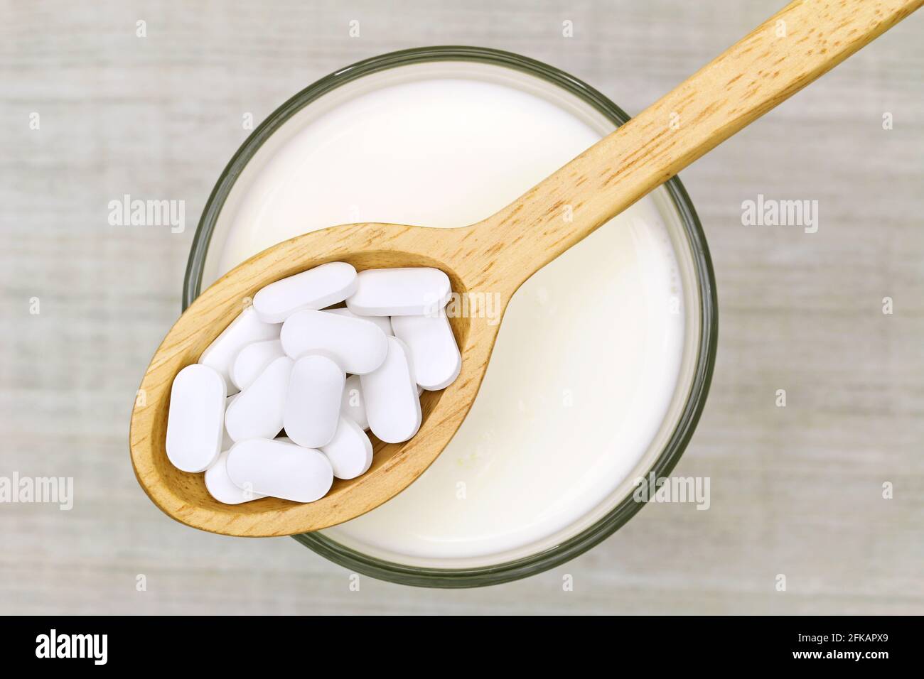 Draufsicht auf einen Holzlöffel aus weißem Calciumcarbonat Die Tabletten  über dem Glas der frischen Milch auf dem Grau Hintergrund Stockfotografie -  Alamy