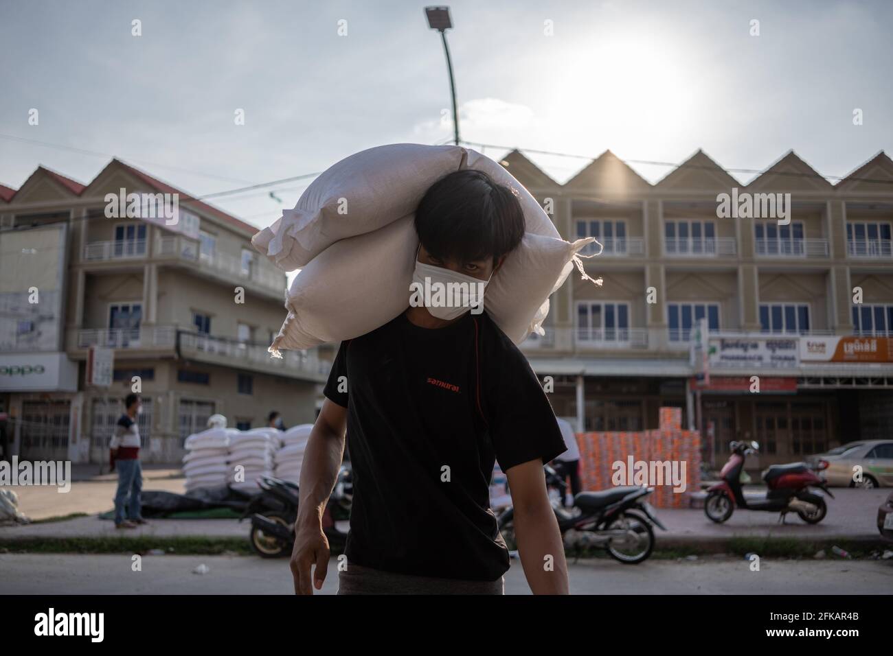 Phnom Penh, Kambodscha. April 2021. Ein Bewohner einer Roten Zone trägt Reissäcke, die während der Coronavirus-Pandemie zu seinem Haus gespendet wurden.Phnom Penh ist nach wie vor in der Blockierung, da Kambodscha drastische Maßnahmen ergreift, um die Ausbreitung des bisher schlimmsten COVID-19-Ausbruchs zu reduzieren. Die Sperre hat viele von ihnen aus der Arbeit gezwungen, darunter Fabrikarbeiter und Marktverkäufer, was die ärmsten Bewohner der Städte in Schwierigkeiten gebracht hat oder nicht in der Lage ist, sich grundlegende Notwendigkeiten zu leisten. (Foto von Andy Ball/SOPA Images/Sipa USA) Quelle: SIPA USA/Alamy Live News Stockfoto