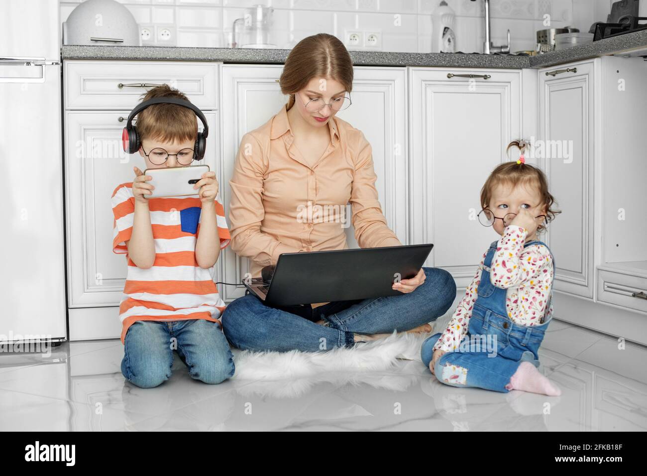 Arbeit im Mutterschaftsurlaub. Mama arbeitet am Laptop. Kinder spielen in der Nähe von Mama. Warmer Boden. Stockfoto