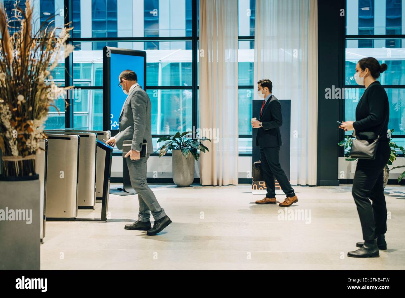 Männliche Unternehmer Scannen Handy U-Bahn-Station zu betreten, während Kollegen, die während der COVID-19 Schlange standen Stockfoto