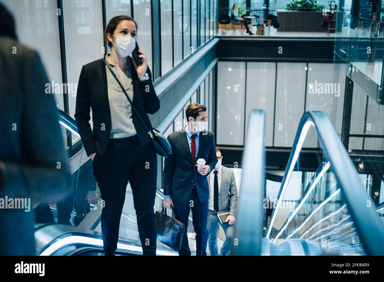 Geschäftsfrau, die über ein Smartphone spricht, während sie sich auf der Rolltreppe nach oben bewegt Während einer Pandemie Stockfoto