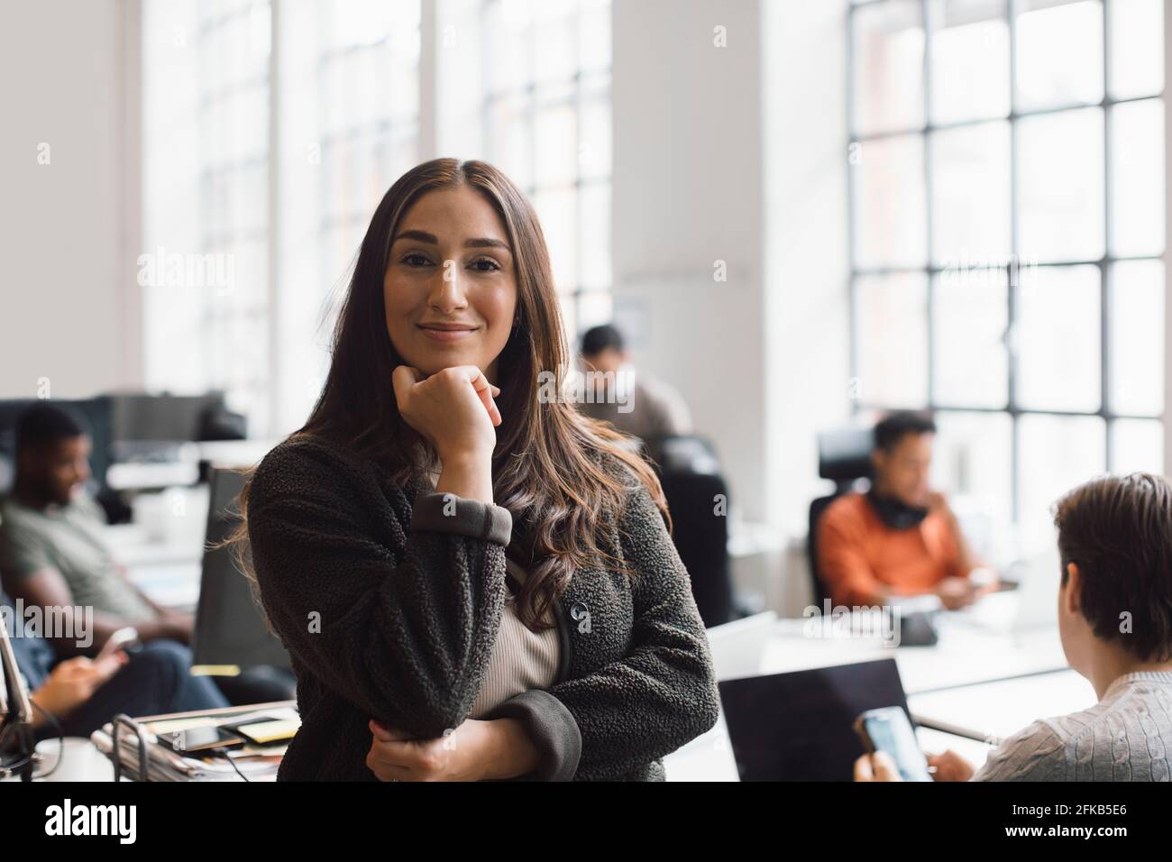 Lächelnde Unternehmerin mit der Hand am Kinn im Kreativbüro Stockfoto