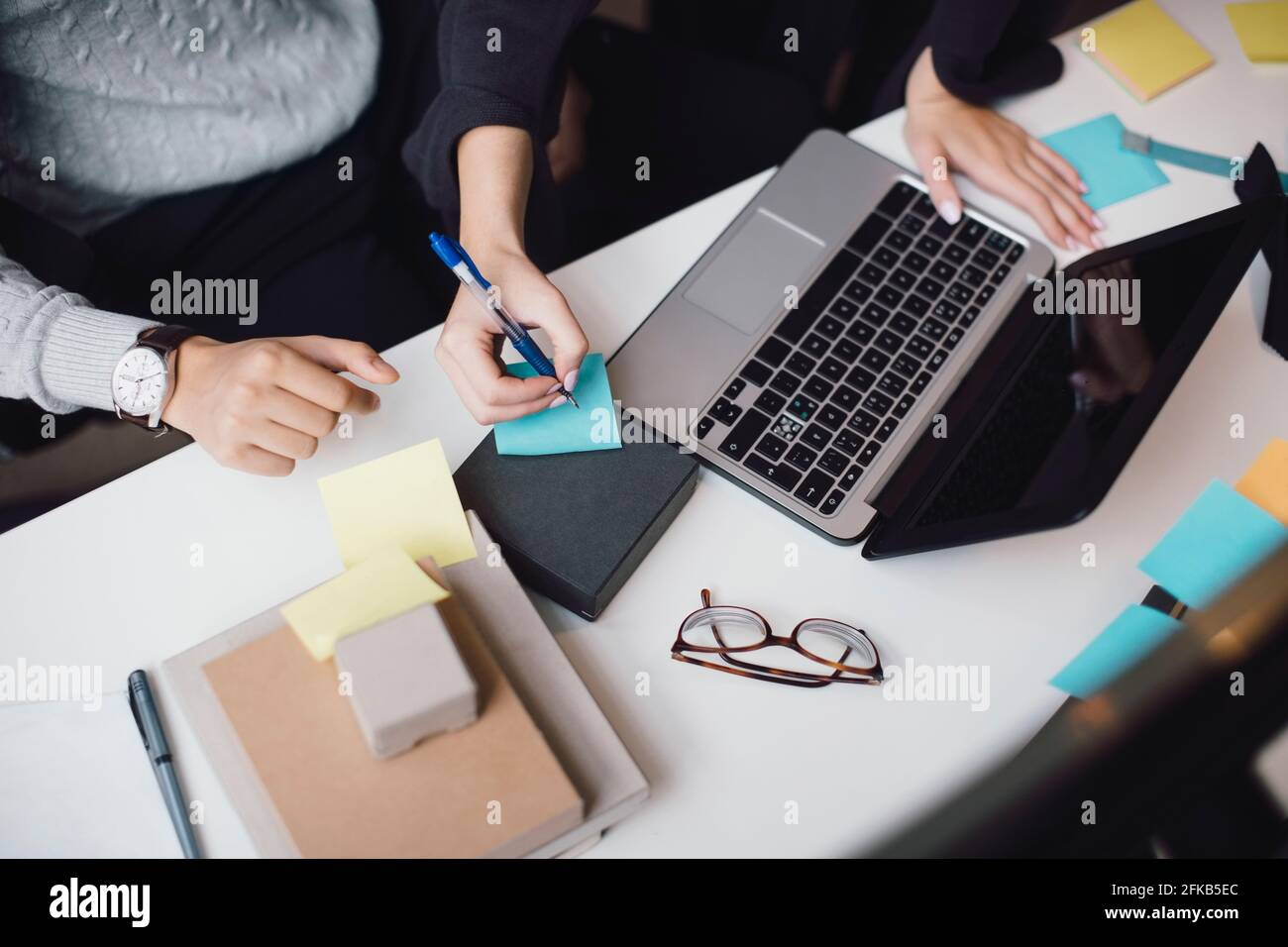 Kurze Hand einer Geschäftsfrau, die per Laptop auf eine Haftnotiz schreibt Am Schreibtisch im Büro Stockfoto