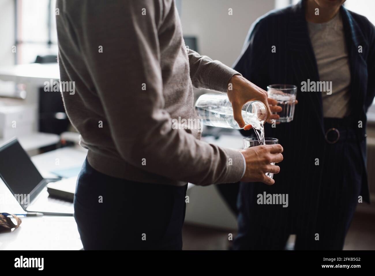 Mittelteil des Geschäftsmannes, der im Büro Wasser in Trinkglas gießt Stockfoto