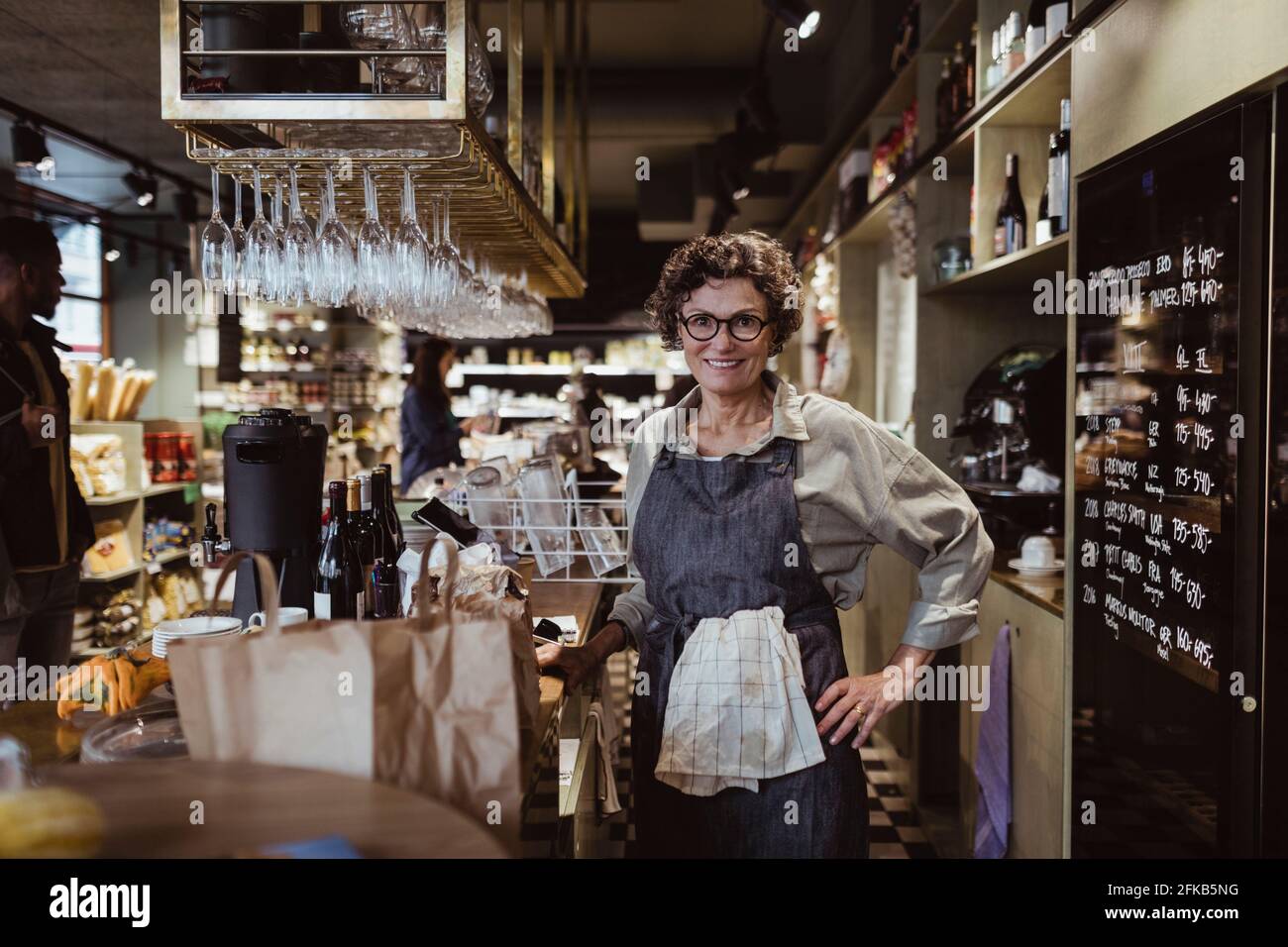 Porträt einer lächelnden Besitzerin mit der Hand auf der Hüfte Feinkostladen Stockfoto