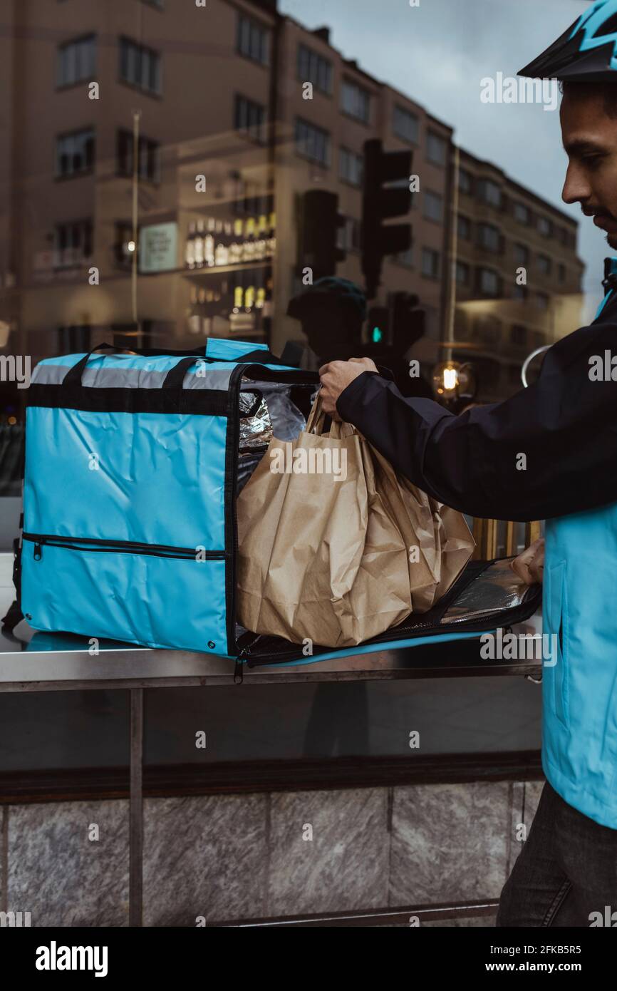 Zugeschnittenes Bild des Lieferers, der die Paketbestellung in den Rucksack legt Außerhalb des Ladens Stockfoto