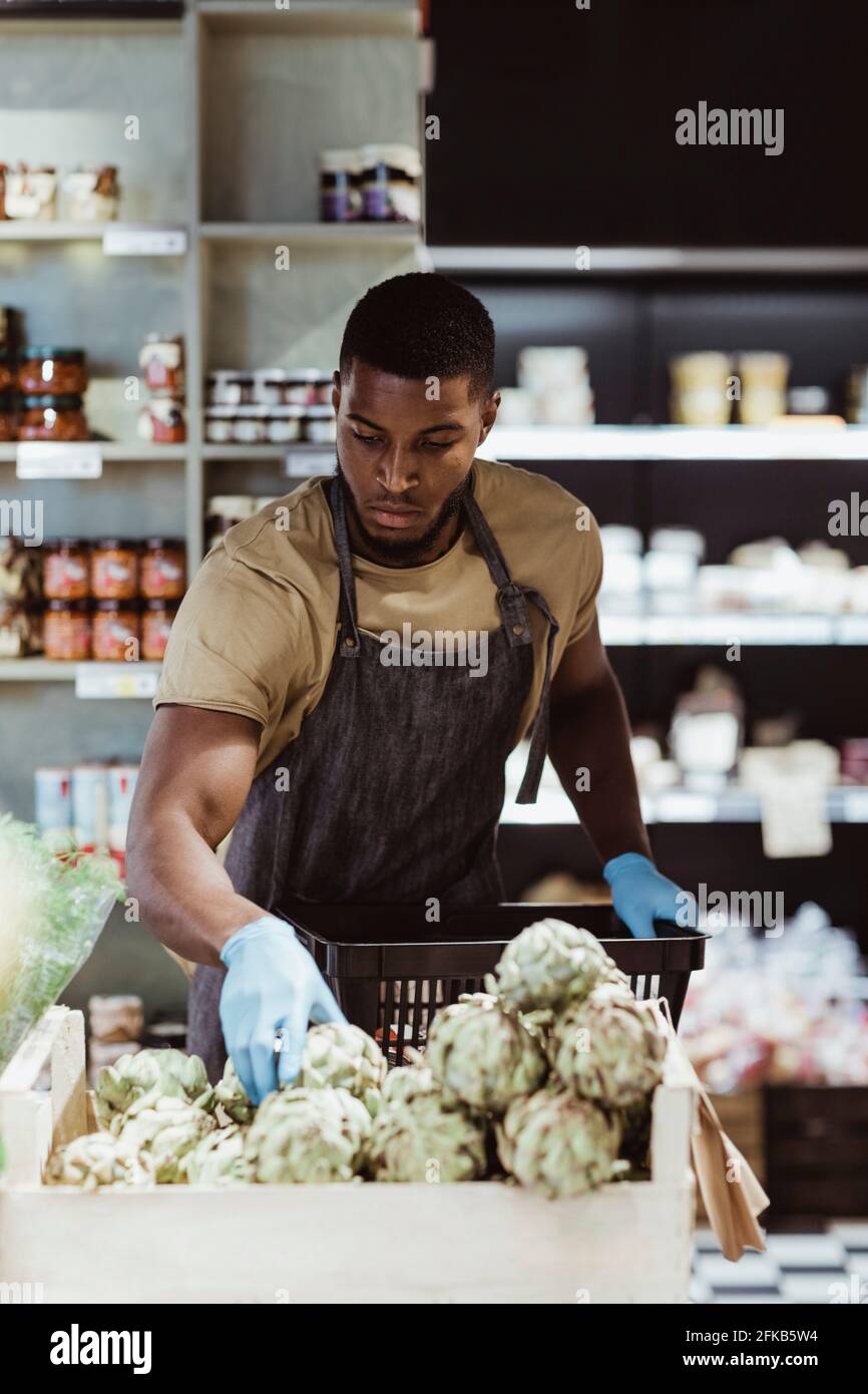 Männlicher Unternehmer, der im Feinkostladen Lebensmittel im Korb anordnet Stockfoto