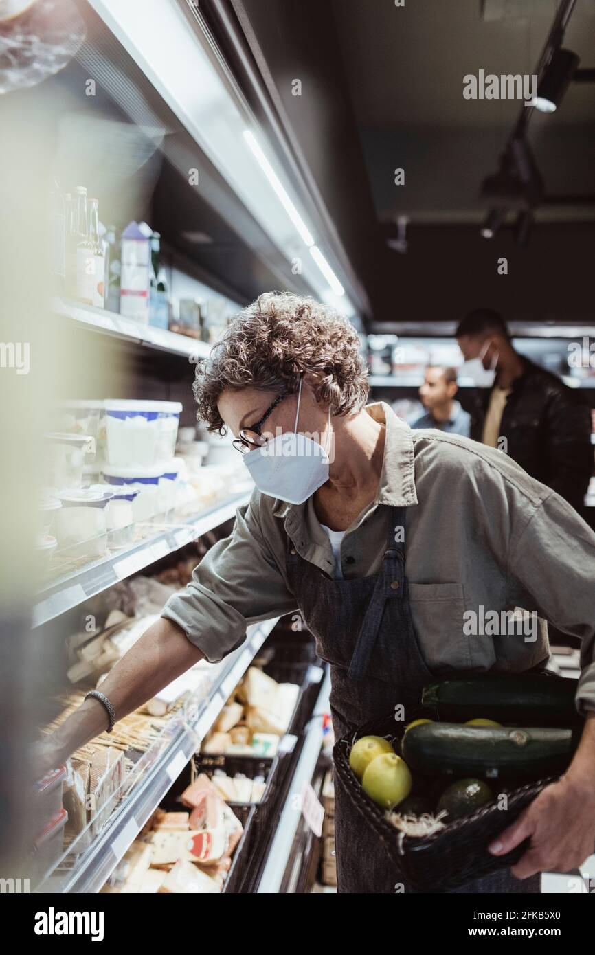 Weibliche Besitzerin, die Lebensmittel auf dem Regal in einem Feinkostladen anordnete Während einer Pandemie Stockfoto