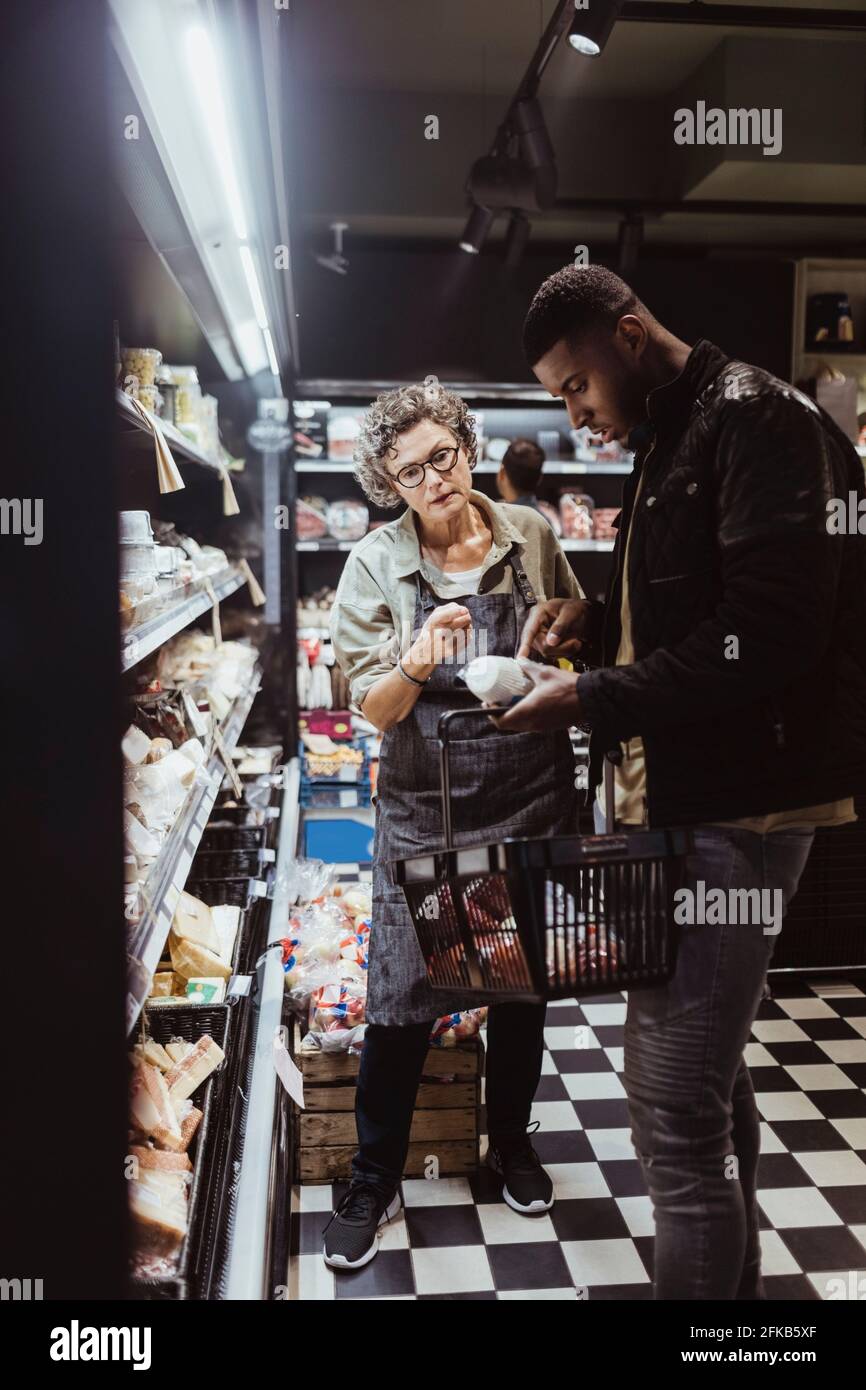 Männlicher Kunde, der das Paketprodukt betrachtet, während die Besitzerin steht Bei Delikatessengeschäft Stockfoto