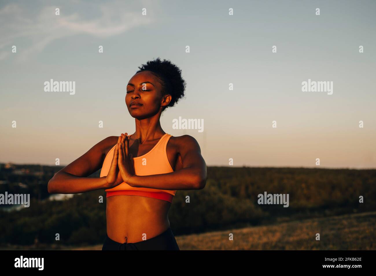 Junge Sportlerin meditiert während des Sonnenuntergangs gegen den Himmel Stockfoto