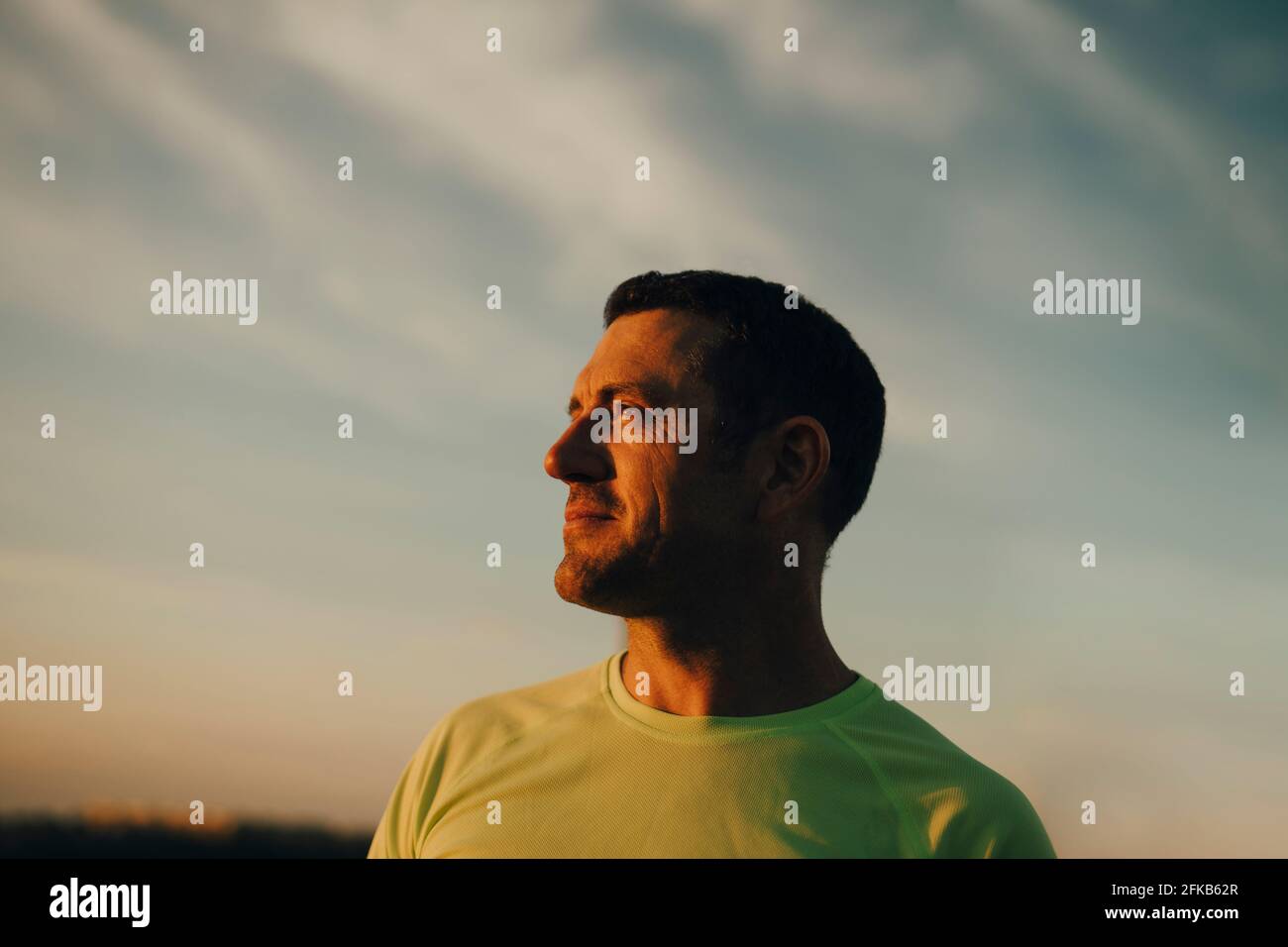 Männlicher Athlet, der während des Sonnenuntergangs gegen den Himmel kontempliert Stockfoto