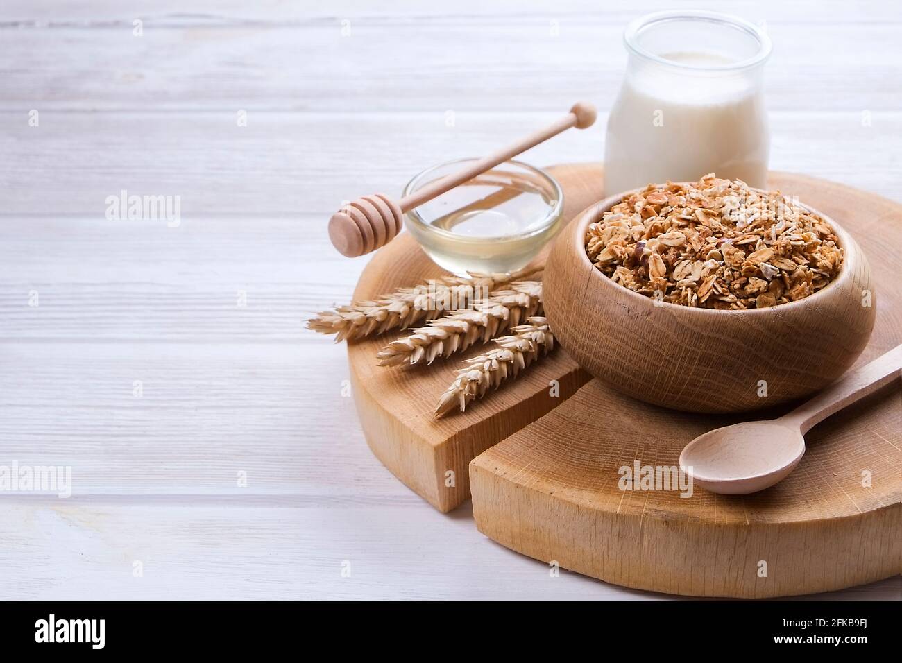 Eine Holzschale mit einer Mischung aus Mandeln, Rosinen, Samen, Cashew, Haselnüssen, Glas Milch und Honig auf weißem Tisch. Vegetarische Ernährung Sport Nutr Stockfoto