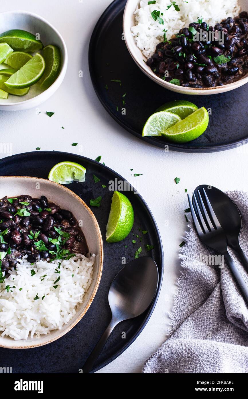 Zwei Schalen mit schwarzen kubanischen Bohnen, serviert mit Reis und Kalk-Keilen. Stockfoto