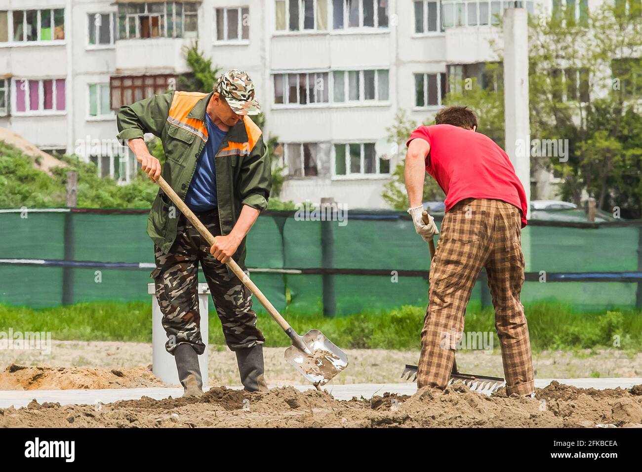 Weißrussland, Minsk - 28. Mai 2020: Männliche Industriearbeiter graben mit Schaufel Erde und nivellieren mit Rechen auf der Baustelle. Stockfoto