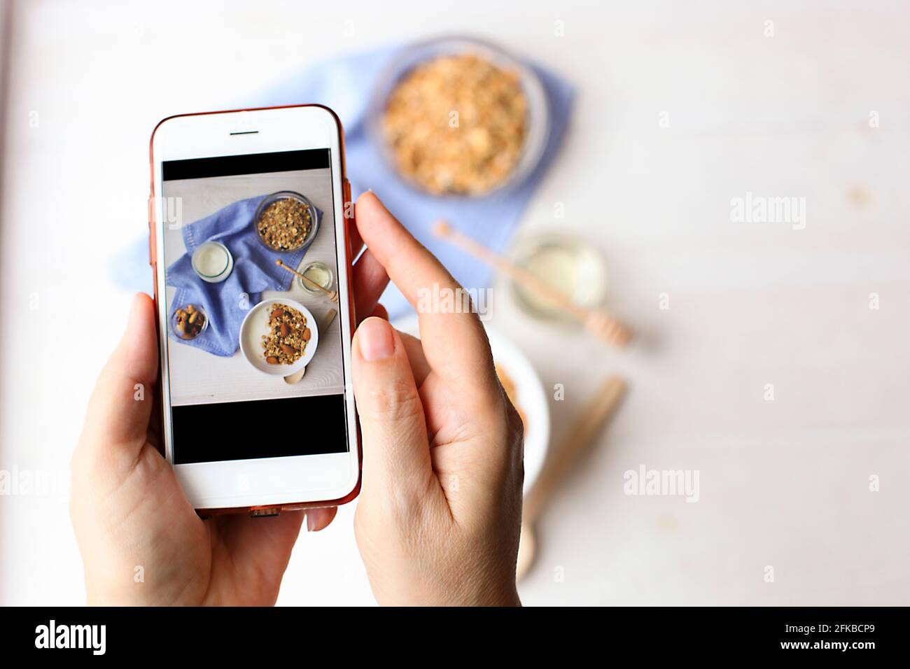 Junge Frau Food-Bloggerin macht Foto für Blog, Bild von Schüssel mit griechischem Joghurt hausgemachtes Müsli, gemischte Nüsse, Mandel, Cashew, Haselnuss. Gesunde Vegetaria Stockfoto