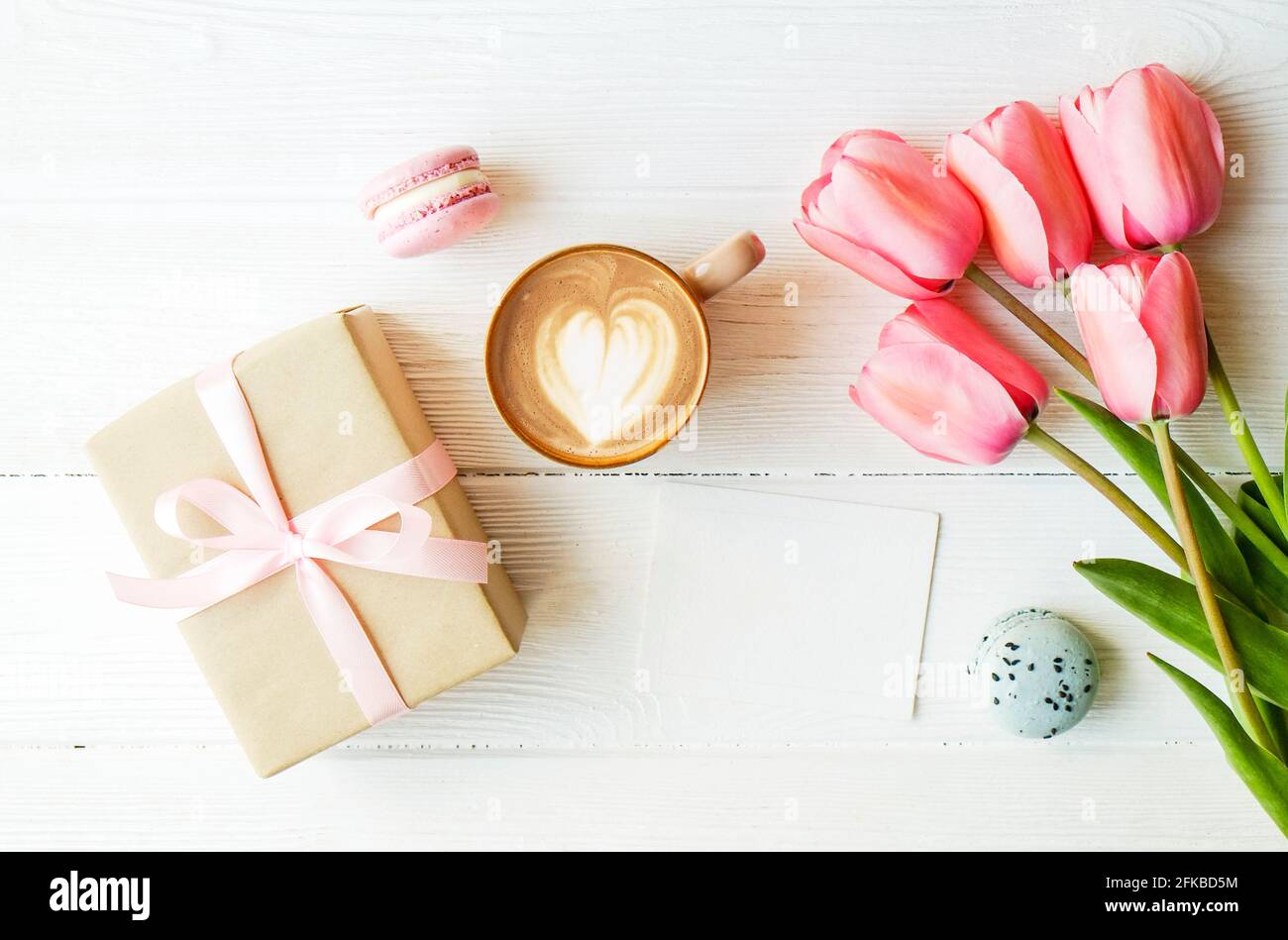 Heidelbeere und Erdbeere aromatisierte französische Macaron-Wüstenkuchen, braune Cappuccino-Kaffeetasse, herzförmige Latte-Kunst, Bastelpapier verpackt präsent Tulpe f Stockfoto