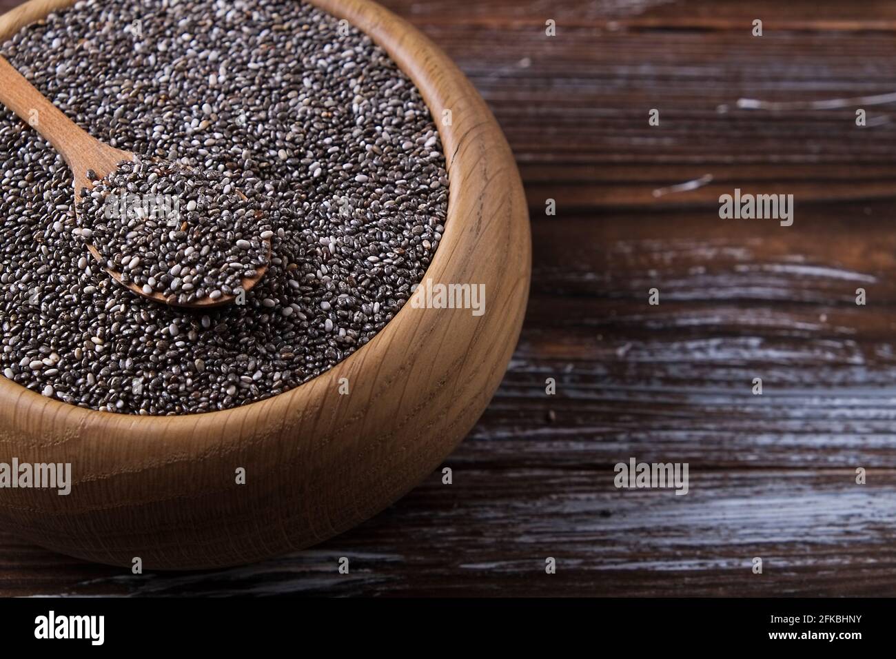 Draufsicht auf Holzschüssel mit Stapel von Bio-schwarzen Chia-Samen und Löffel auf geronged Holz strukturierte Tisch. Gesunde nahrhafte vegane Ernährung suppliment. Clea Stockfoto