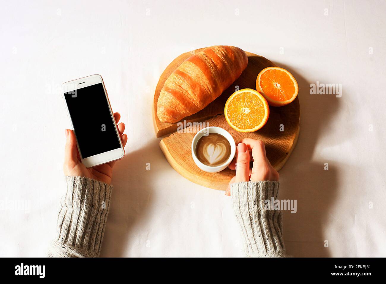 Über dem Kopf geschnittene Aufnahme einer Frau, die ein Mittagessen mit Croissants und Kaffee hatte und ihr Telefon scrollte. POV. Stockfoto