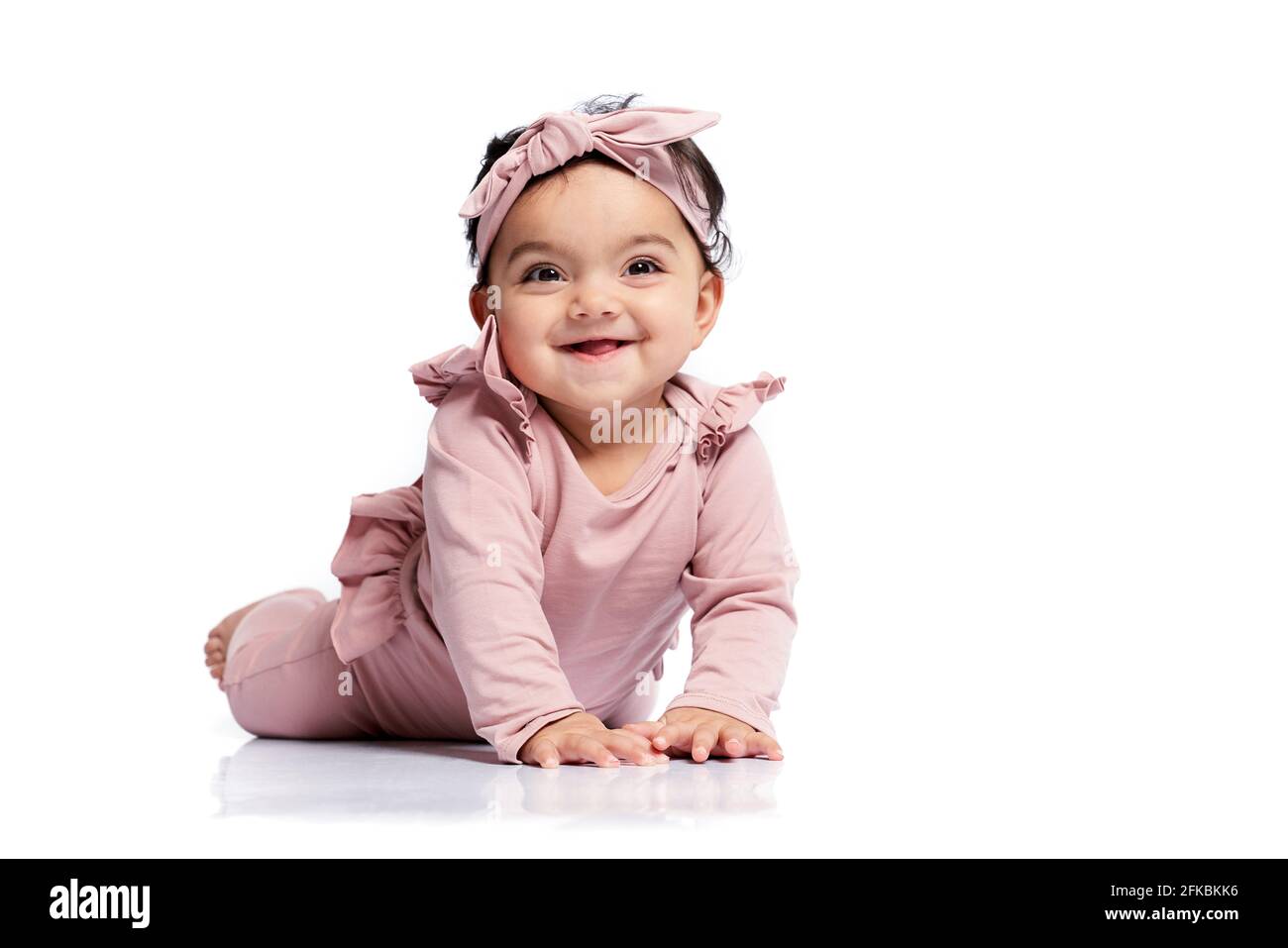 Niedliches weibliches Baby im schönen rosa Outfit, lächelnd mit offenem Mund und aufblickend. Attraktives kleines Baby, das auf dem Boden kriecht und posiert, isoliert auf Weiß Stockfoto