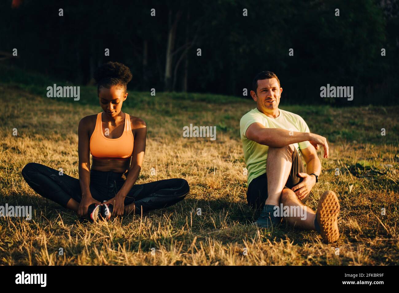 Sportler und Sportlerin machen Entspannungsübungen, während sie auf Gras sitzen Bereich Stockfoto