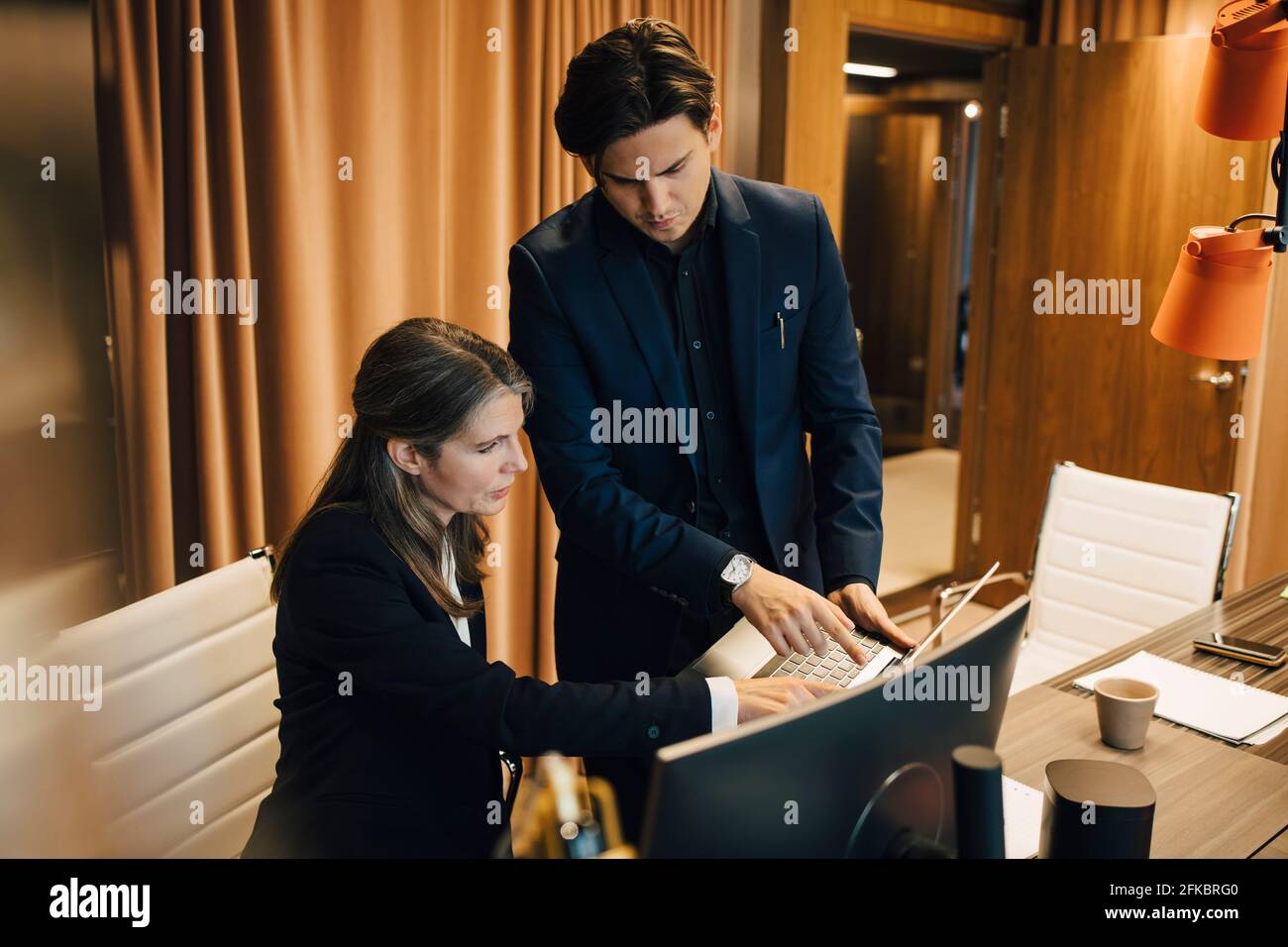 Männlicher Unternehmer, der mit einer Rechtsanwältin über einen Laptop an Bord diskutiert Zimmer im Büro Stockfoto