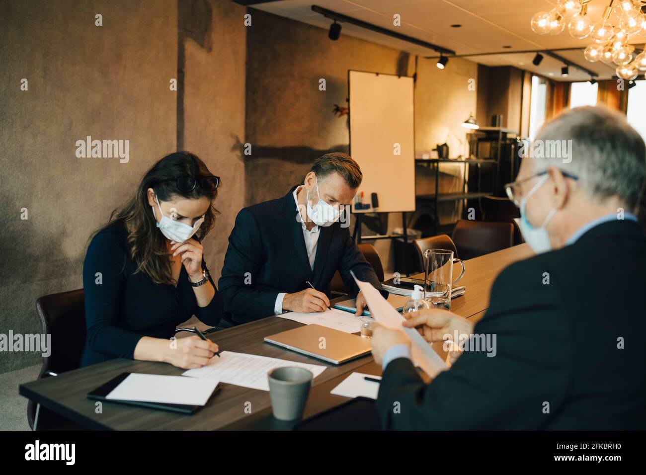 Männliche und weibliche Kollegen schreiben auf Papier im Vorstandszimmer Während der COVID-19 Stockfoto