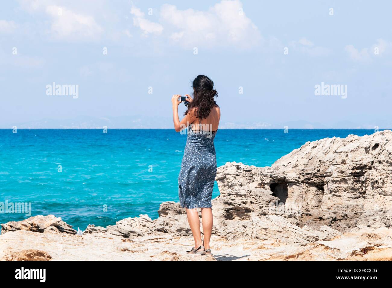 Junge Reisende fotografiert mit ihrem Smartphone den Horizont über dem Meer und genießt ihren Sommerurlaub auf der Insel Formentera, ein wahrer Urlaub pa Stockfoto