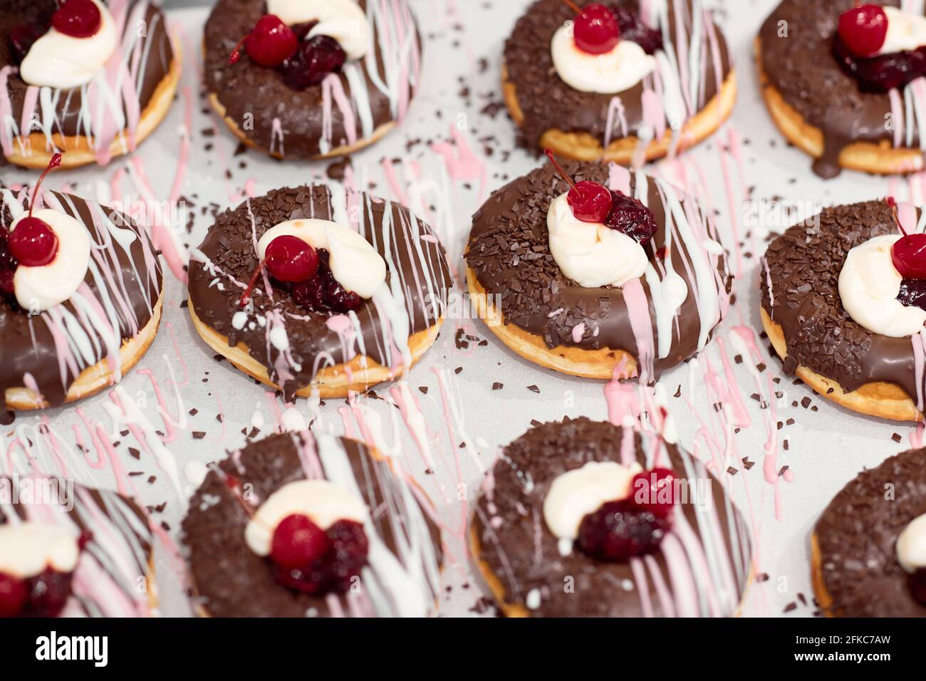 Nahaufnahme von köstlichen Donuts von unwiderstehlichem Aussehen mit Schokoladenüberzug und Kirsche auf der Oberseite auf dem Tablett bereit für eine Konditorei. Gebäck, Dess Stockfoto