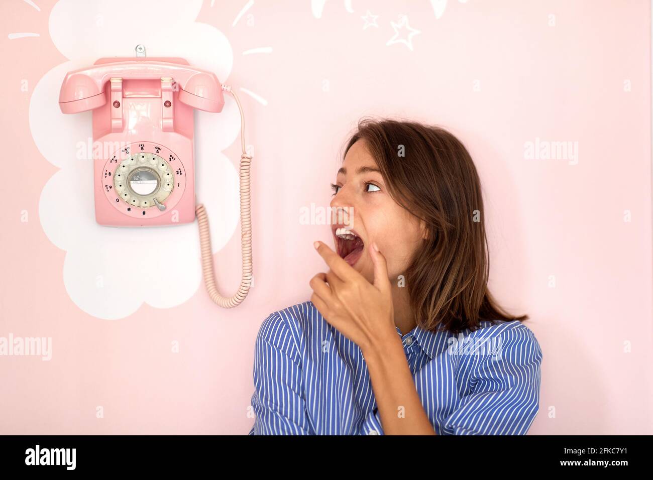 Ein schönes junges Mädchen, das neben einem Retro-Telefon steht, das in einer Konditorei an der Wand hängt und in einer angenehmen Atmosphäre auf einen Anruf wartet. Gebäck Stockfoto