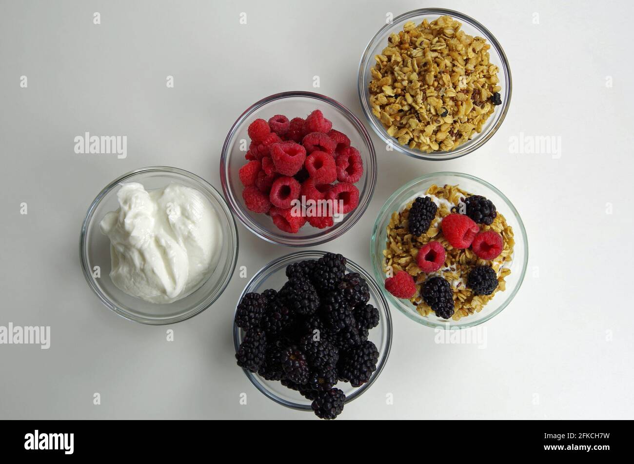 Gesunde Zutaten für die Zubereitung von Snacks oder Mahlzeiten, darunter Joghurt, Himbeeren, Brombeeren und Müsli Stockfoto