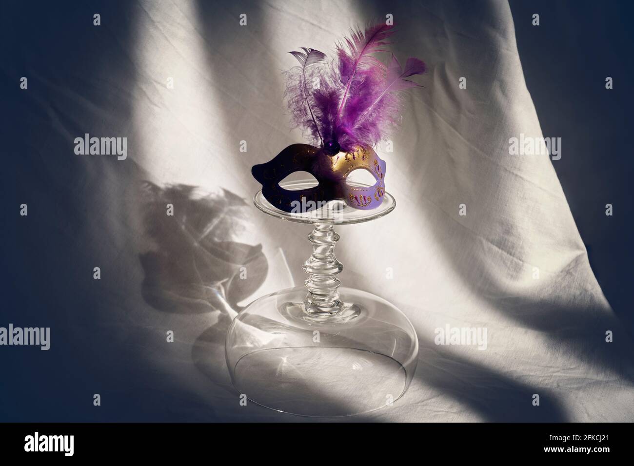 Ein umgedrehtes Champaign-Glas und eine Maskerade darauf. Schöne Schatten im Hintergrund geben Rätsel auf Stockfoto