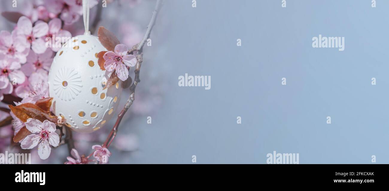 Dekoratives Osterei, das an blühenden Kirschbäumen mit rosa Blüten hängt. Osterhintergrund. Blüht an einem sonnigen Frühlingstag. Selektiver Fokus Stockfoto