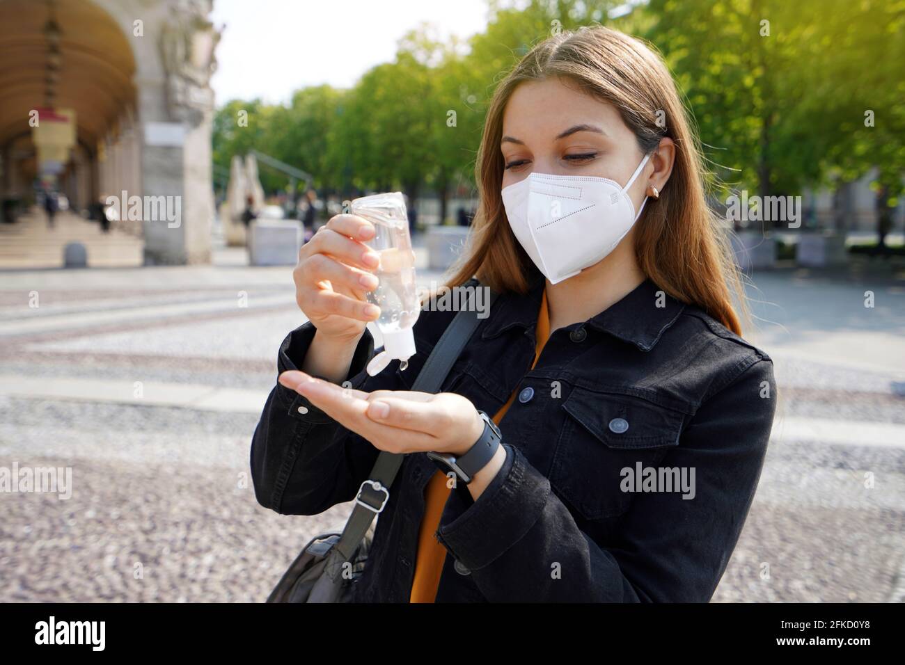 Porträt einer schönen jungen Frau, die eine KN95 FFP2 Schutzmaske trägt und Alkoholgel verwendet, um ihre Hände auf der Straße der Stadt zu desinfizieren. Hygiene und Gesundheitsversorgung con Stockfoto