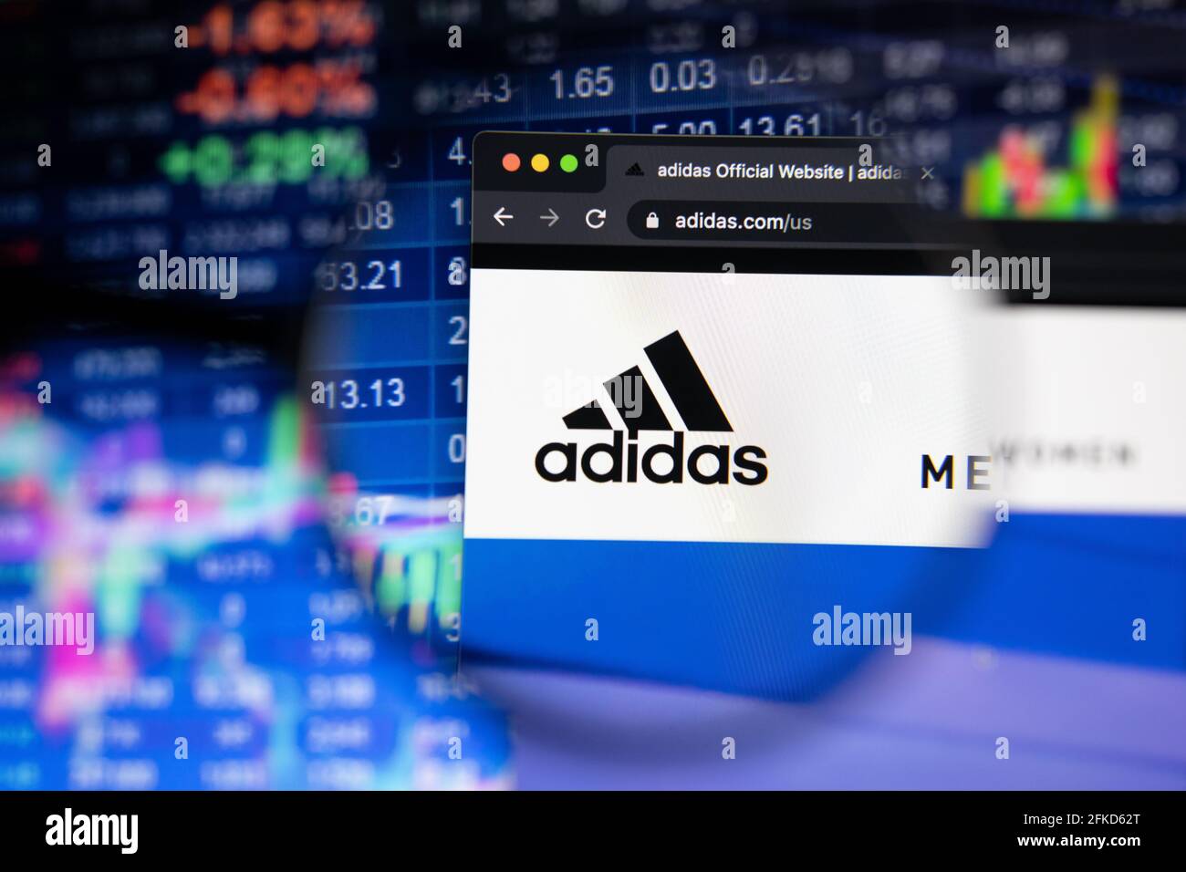 Adidas Firmenlogo auf einer Website mit verschwommenen Börsenentwicklungen im Hintergrund, die auf einem Computerbildschirm durch eine Lupe gesehen werden Stockfoto