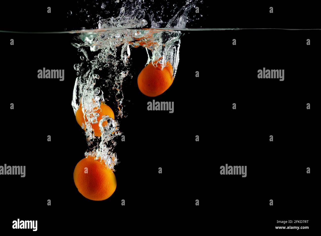 Drei Mandarinen fallen auf schwarzem Grund ins Wasser Stockfoto