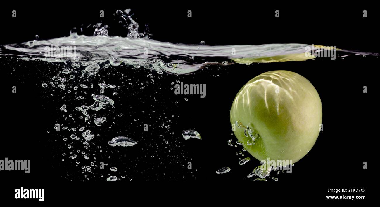 Frischer Apfel fällt in Wasser mit Luftblasen, schwarzer Hintergrund, Kopierraum Stockfoto