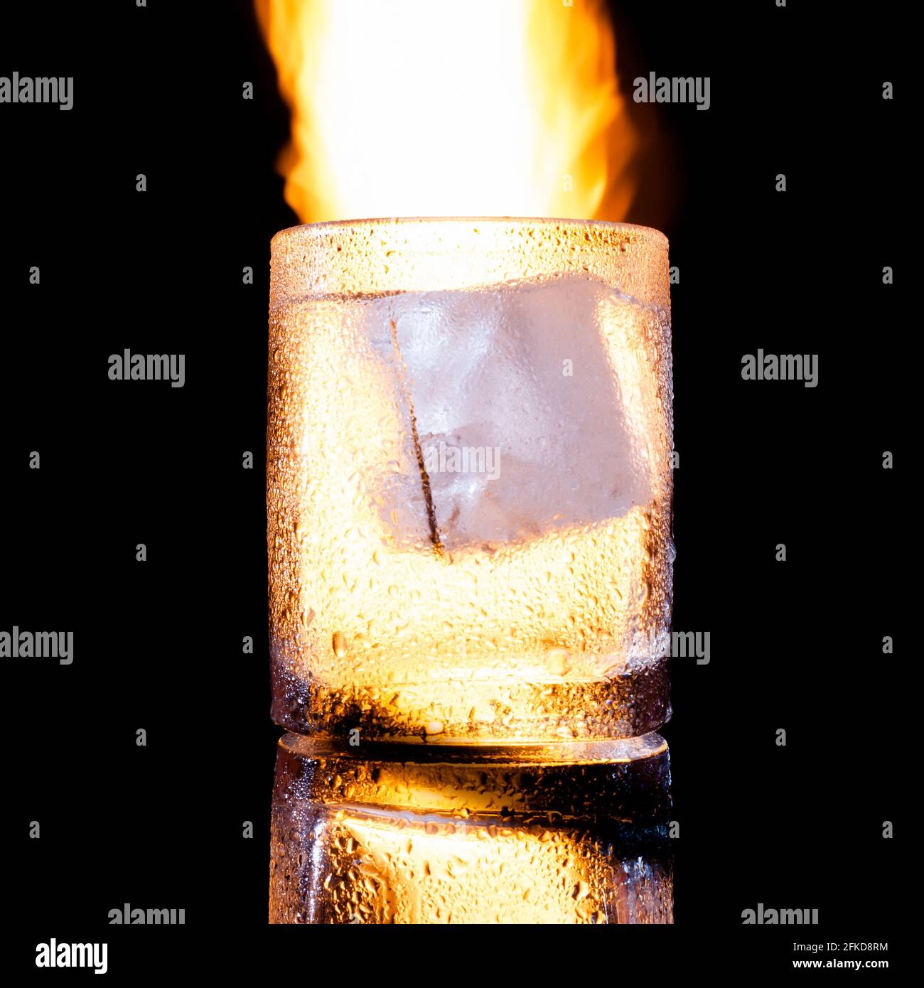 Glas mit einem Stück Eis vor dem Hintergrund von Feuer Stockfoto